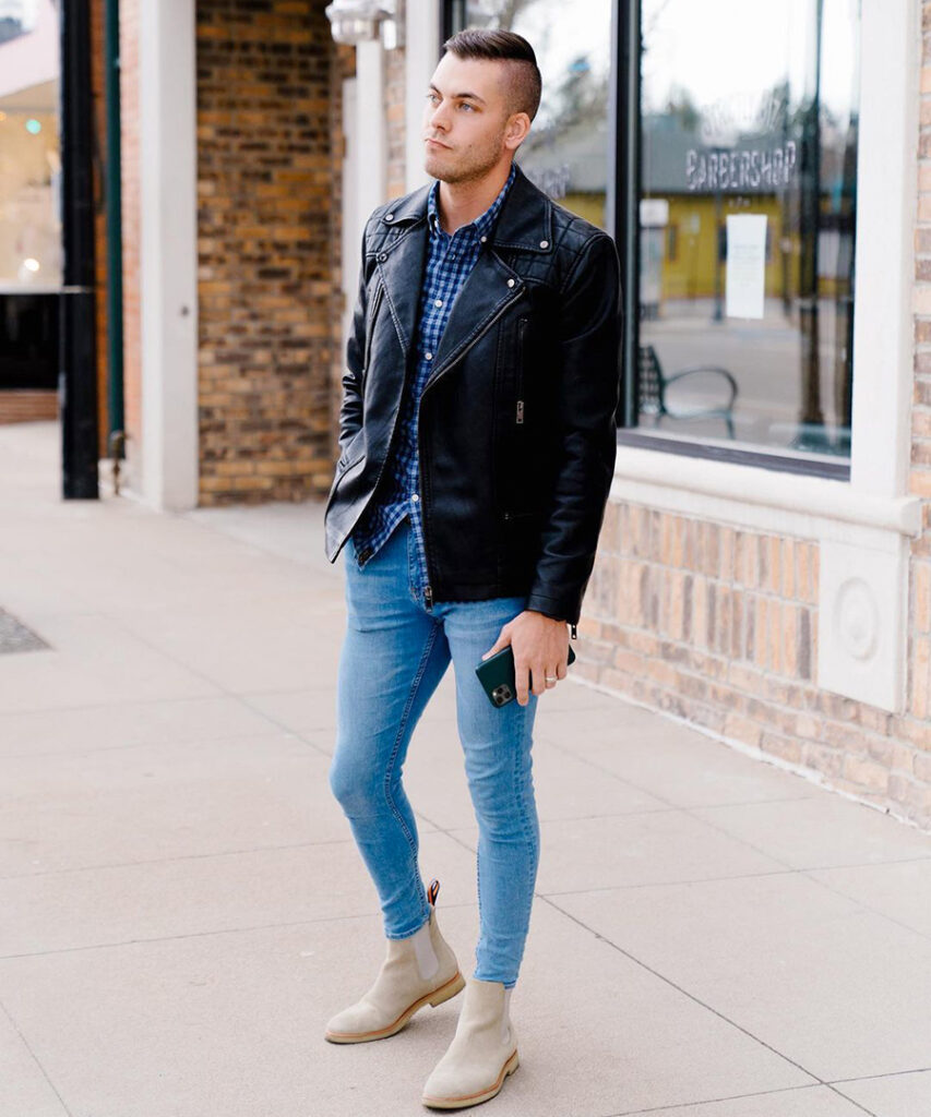 Black leather jacket, blue patterned shirt, light blue jeans, and tan suede Chelsea boots