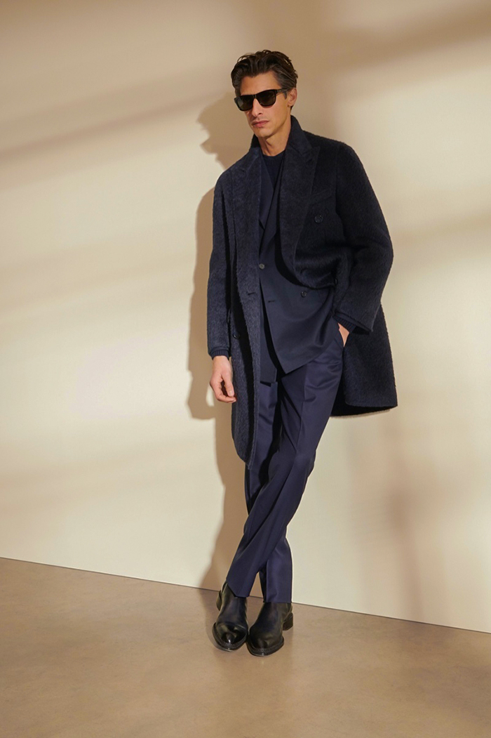 Black overcoat, navy suit, crew neck sweater, and Chelsea boots outfit