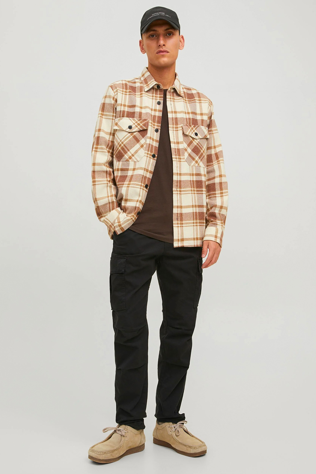 Brown plaid shirt jacket, brown t-shirt, black cargo pants, and light brown desert boots outfit