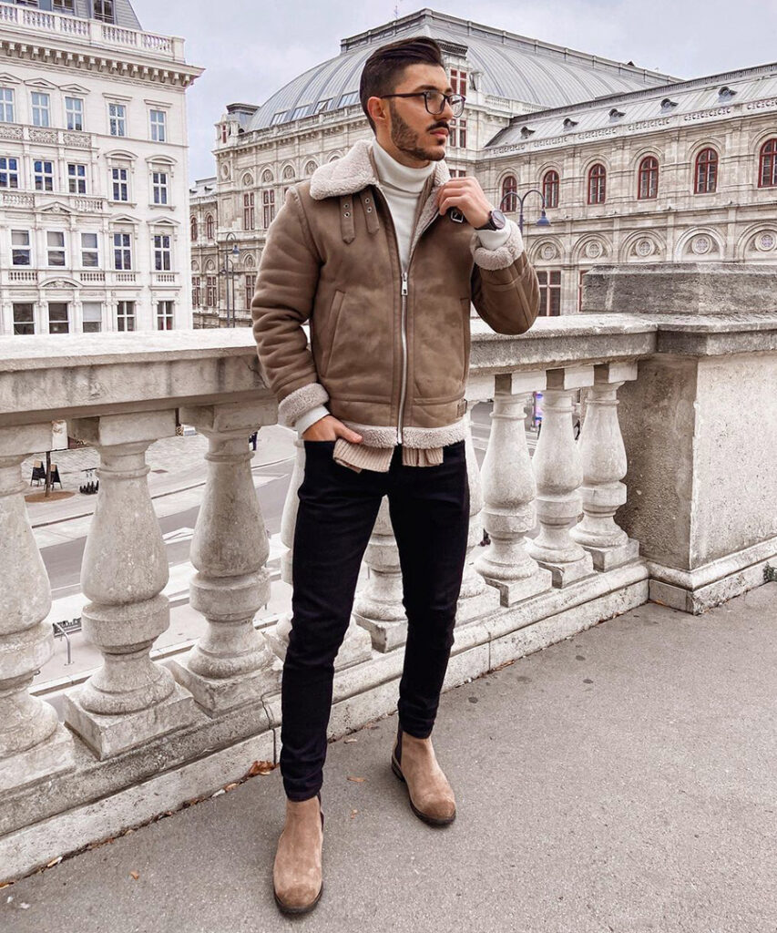 Brown shearling jacket, beige turtleneck, black jeans, and brown suede Chelsea boots