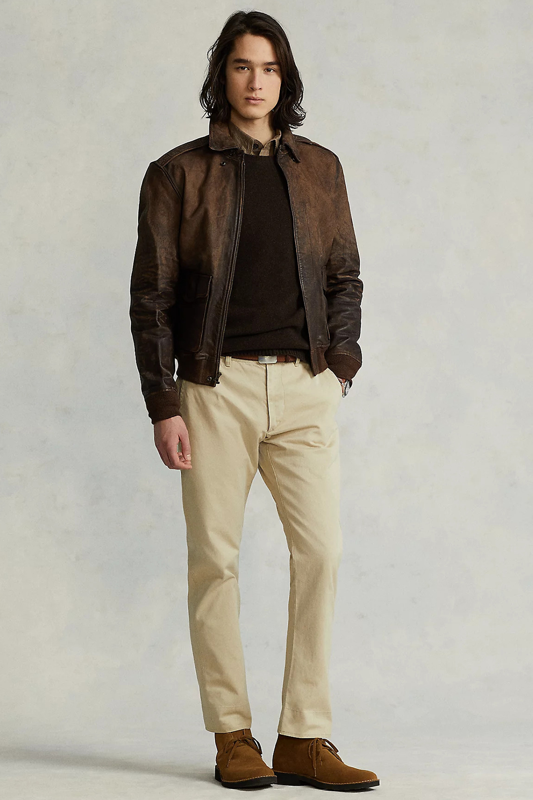 Dark brown leather bomber jacket, light brown shirt, brown sweater, khaki chinos, and brown suede desert boots outfit