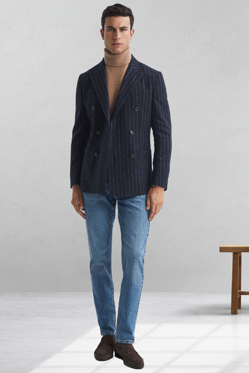 Navy pinstripe double-breasted blazer, tan turtleneck, blue jeans, and brown loafers outfit