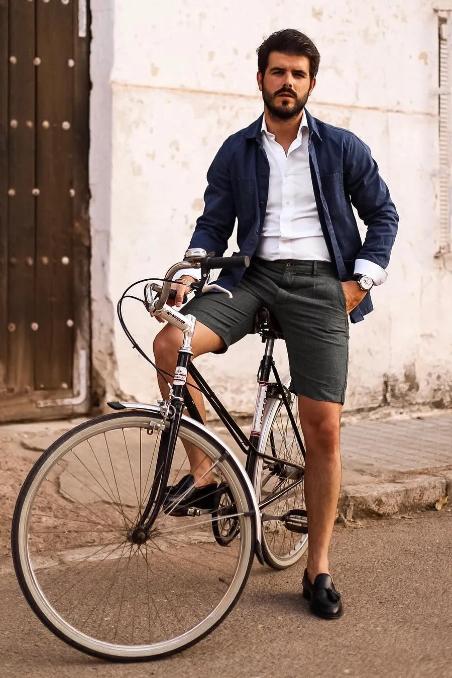 Wear a navy shirt jacket, white long-sleeve shirt, gray denim shorts, and black loafers