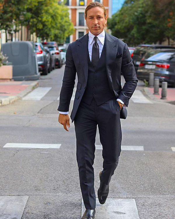 Wearing a black three-piece suit, black tie, white dress shirt and black leather Chelsea boots