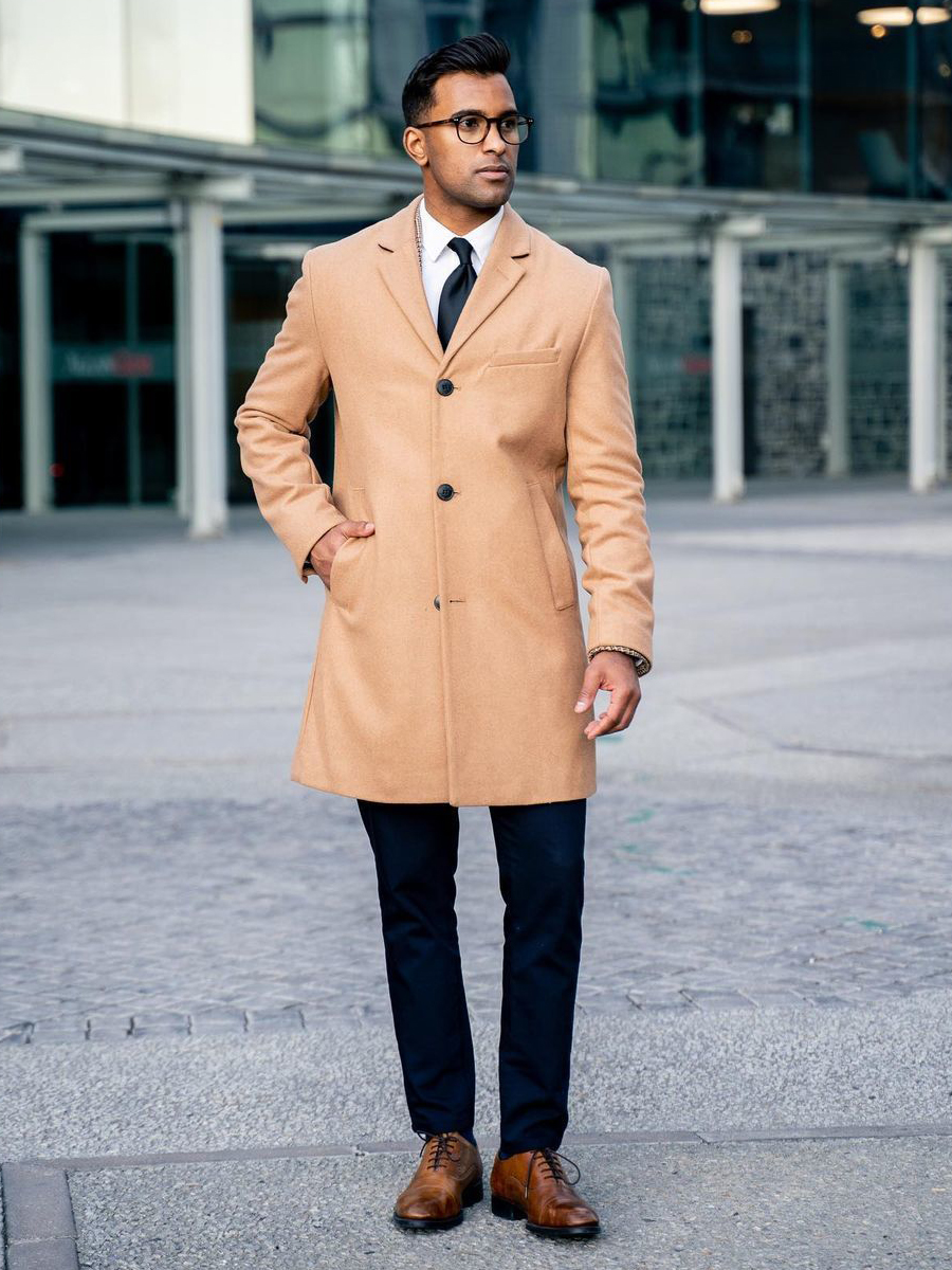 Wearing a camel overcoat, white dress shirt, navy chinos, and brown oxford shoes