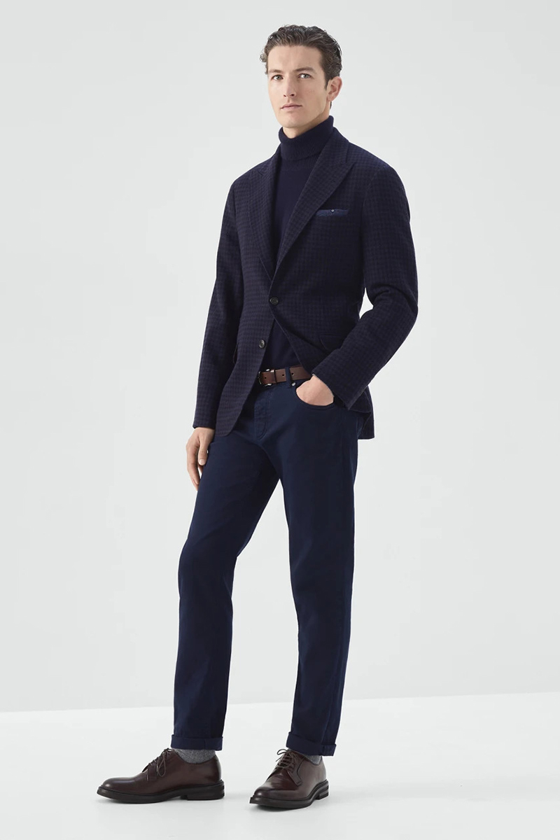 Wearing a navy houndstooth blazer, navy turtleneck, blue chinos, and brown derby shoes