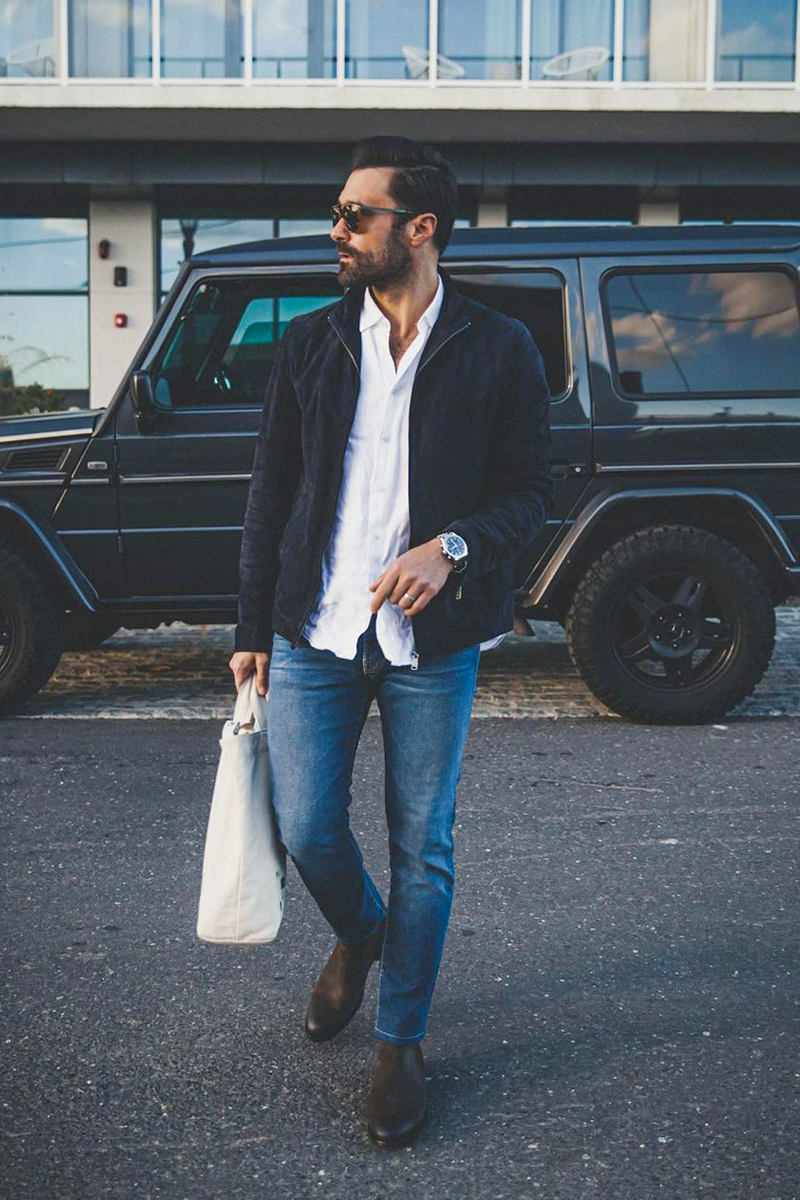Wearing a navy suede bomber jacket, white long sleeve shirt, blue jeans, and dark brown Chelsea boots